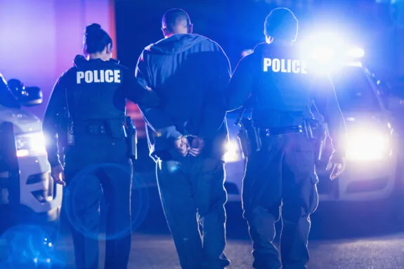 Rear view of two multiracial police officers arresting a criminal suspect